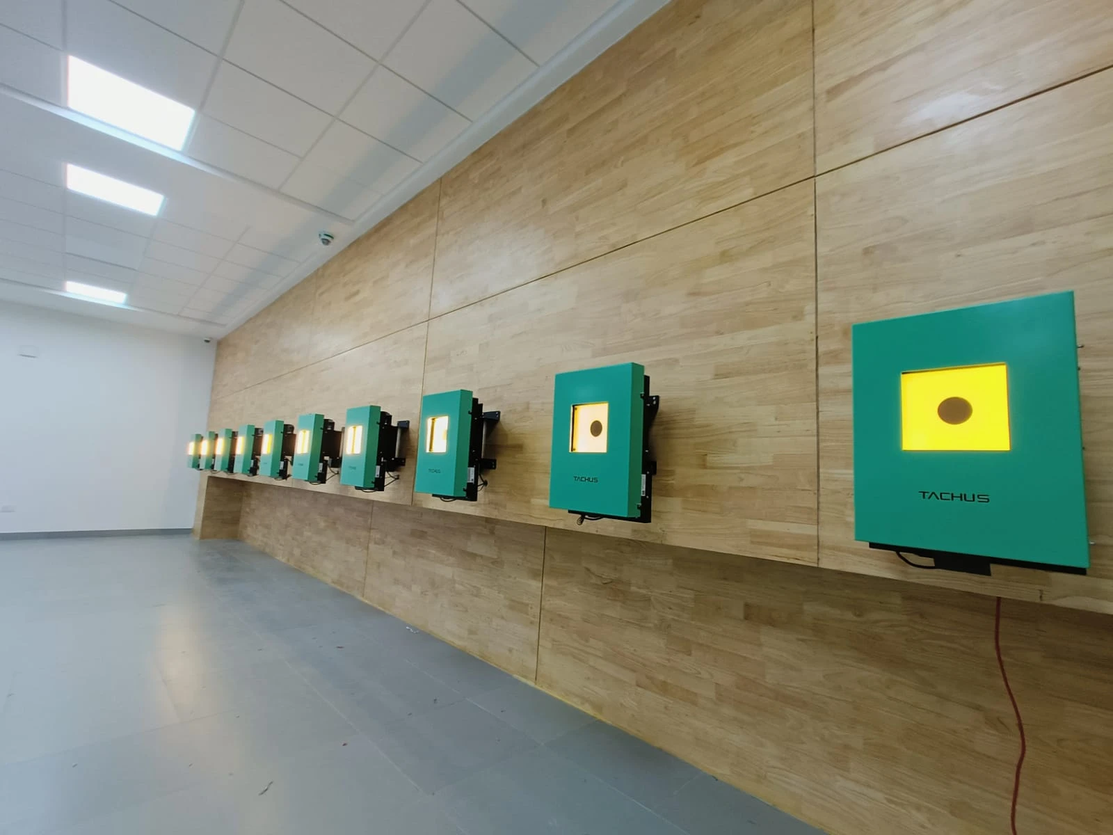 A row of illuminated Tachus electronic targets installed along an institutional range with wood panelling