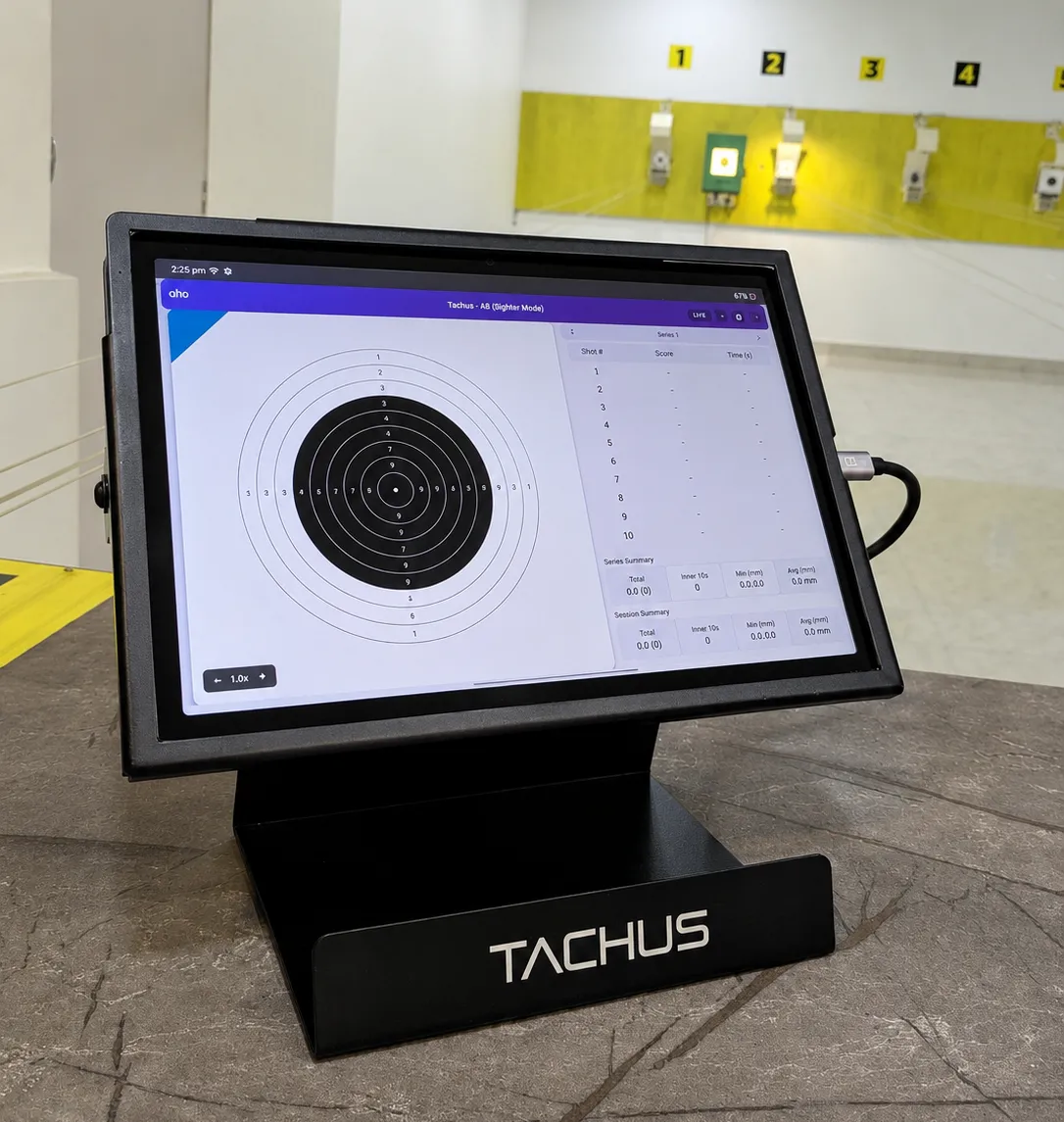 TACHUS display station showing the scoring app's target view and shot table, with shooting lanes in the background
